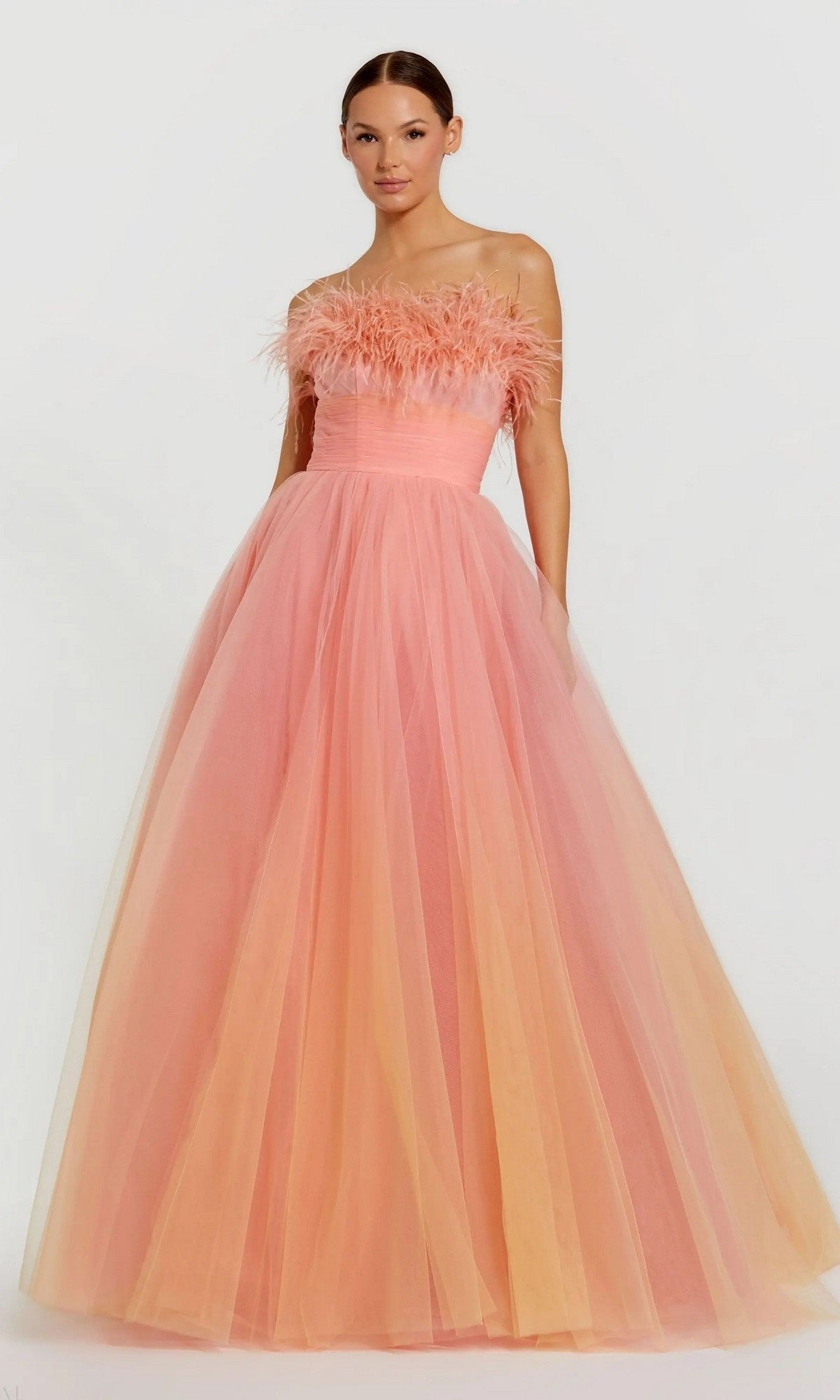 A woman stands against a plain light background wearing the Mac Duggal Long Formal Dress 20557, featuring an ombre feather design, strapless bodice, and full tulle skirt.